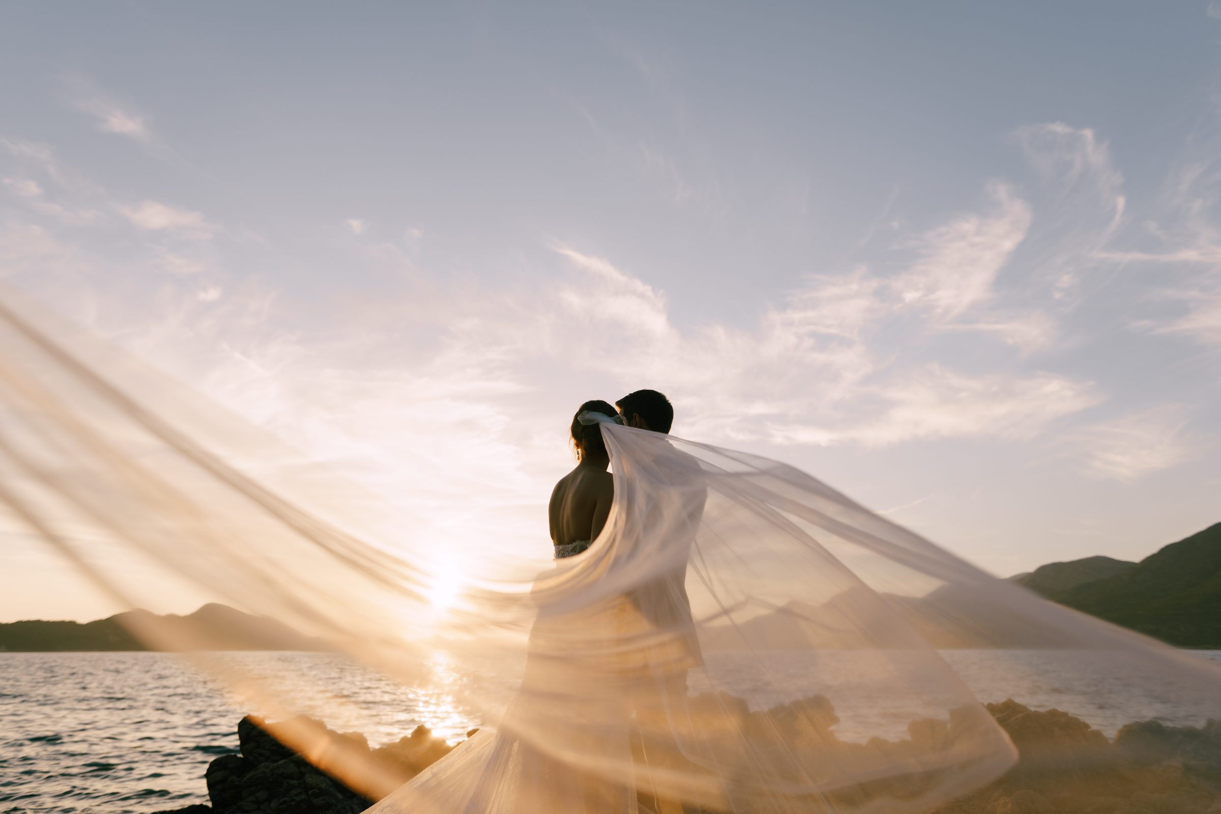 Bride and groom at sunset by Lake Geneva with the veil flowing in the wind