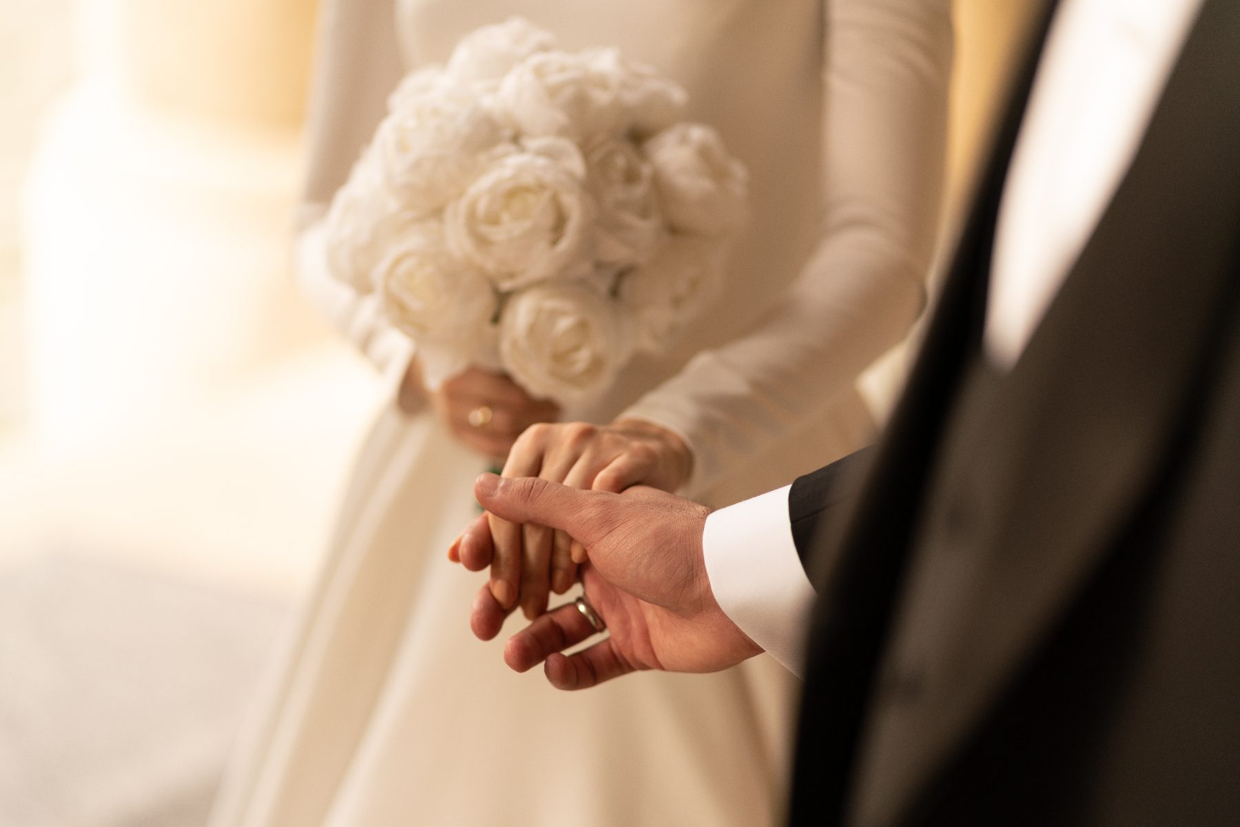 Couple élégant se tenant la main à l'autel, la mariée tenant un bouquet de roses blanches